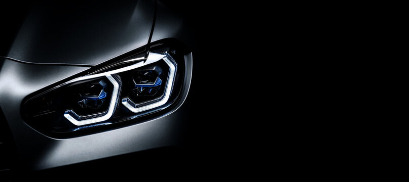 Luxury car LED headlight closeup with U-shaped DRL and dual blue projectors on gray body dark background