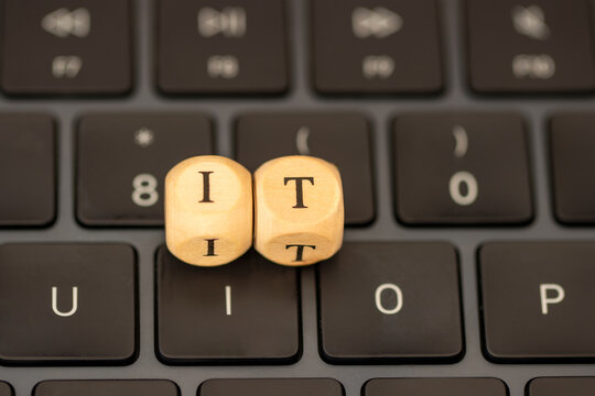 Wooden letter blocks spelling IT, shortage of Information Technology, placed on a computer keyboard.
