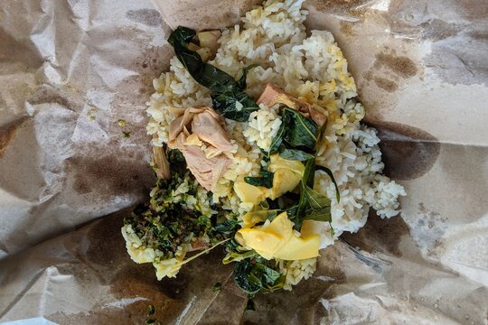 Authentic Indonesian Nasi Bungkus wrapped in brown paper with jackfruit curry, cassava leaves, and green chili sambal.