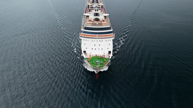 Top down aerial view of a cruise ship bow with green helipad sailing through deep dark waters, June 2025