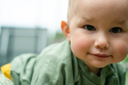 Happy baby with chubby cheeks sitting in garden outdoors with heartwarming smile. Infant enjoying nature and joyful moment with innocent expression. Chubby cheeked little one resting in green yard