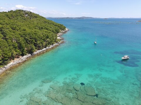 Adriatic sea rocky coastline with cleen turqouise sea and boats in the distance, aerial photo