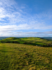 Fototapeta premium Rolling green hills and fields stretch across the Irish countryside under a bright blue sky with soft clouds