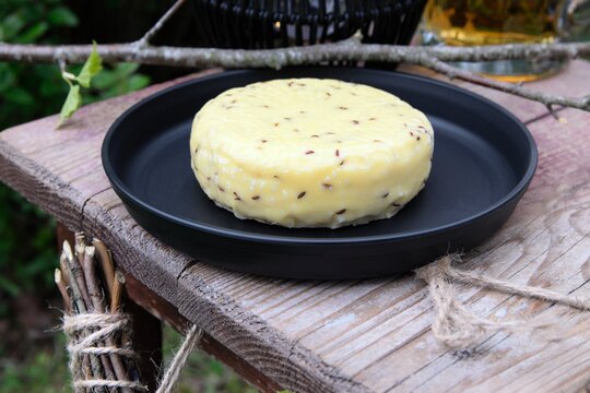 Close-up view of traditional Latvian caraway cheese on a black tray and wooden stool with beer in the background