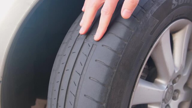 Close-up of a hand pointing at a worn and damaged car tire, checking for safety