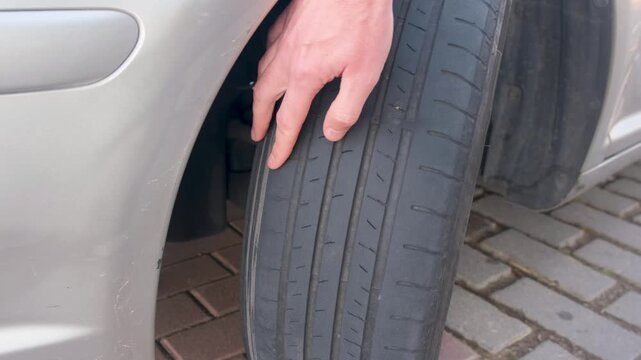 Male hand checking the worn tread on an old car tire, highlighting road safety and maintenance concepts
