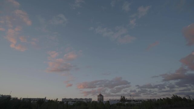  Pink tinged clouds drifting over a dark city skyline at sunset
