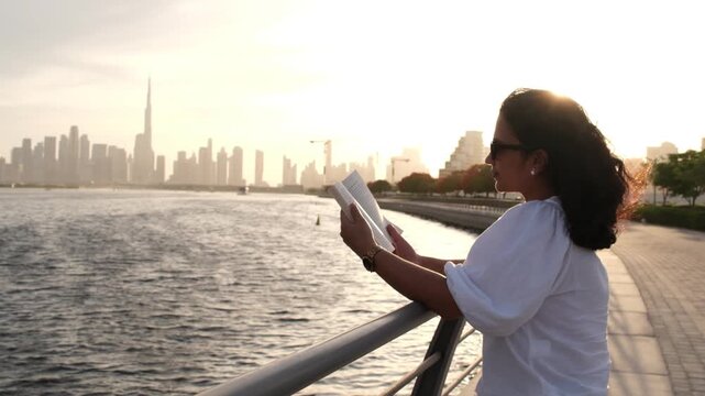 Female reader standing by Dubai waterfront with inspiring city skyline at sunset