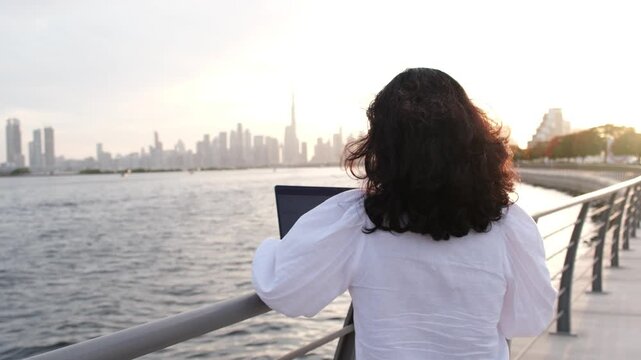 Digital entrepreneur using laptop beside Dubai skyline during golden hour waterfront footage