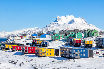 Contemporary greenlandic neighborhood with blue, green, red and yellow colorful Inuit house blocks on rocky hillside beneath a striking mountain snow peak, Nuuk, Sermersooq, Greenland © vadim.nefedov
