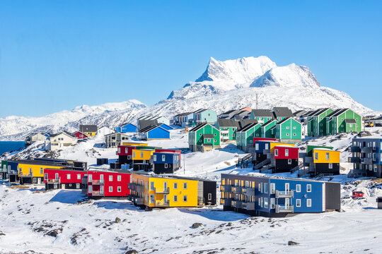 Contemporary greenlandic neighborhood with blue, green, red and yellow colorful Inuit house blocks on rocky hillside beneath a striking mountain snow peak, Nuuk, Sermersooq, Greenland