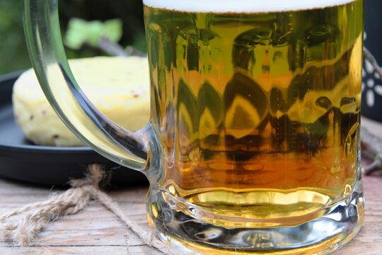 Close-up of a mug of lager beer, traditional caraway cheese on a black tray in the background, outdoor lighting 