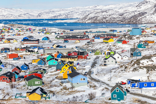 Colorful arctic residential neighborhood with bright wooden Inuit houses scattered across snowy hills above the coast of winter fjord, Narsaq, Kujalleq municipality, Greenland