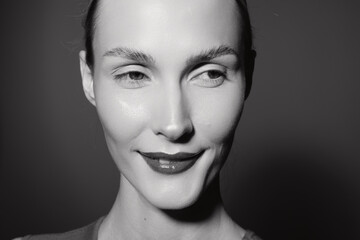 Fototapeta premium Close-up portrait of a young white woman with pale skin smiling softly. Black and white studio photo emphasizing natural beauty and subtle positive emotion in monochrome.