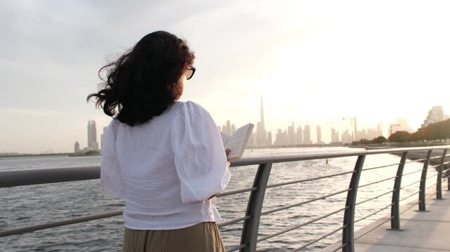 Woman reading outdoors with calm luxury lifestyle and Dubai skyline at golden hour 4k video