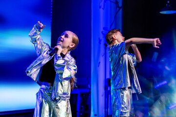Girl and boy dancing on stage under stage light. Young dancers performing in shiny costume. Music show concert
