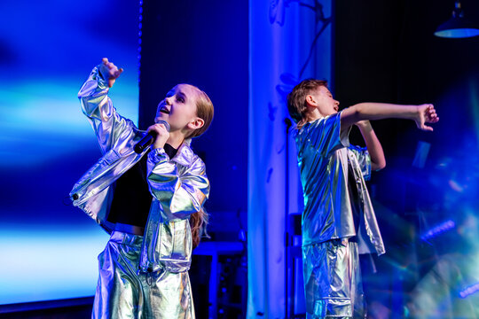 Girl and boy dancing on stage under stage light. Young dancers performing in shiny costume. Music show concert