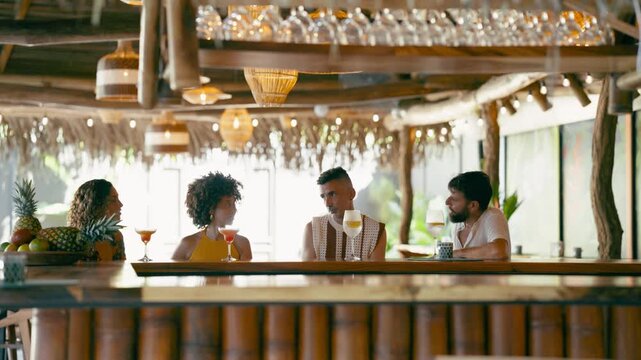 Diverse group of young adult friends socializing and drinking cocktails at a tiki style bar. Happy people enjoying their vacation at a resort