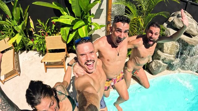 Four excited friends holding a camera taking a selfie video before jumping backwards together into a swimming pool during a summer vacation party