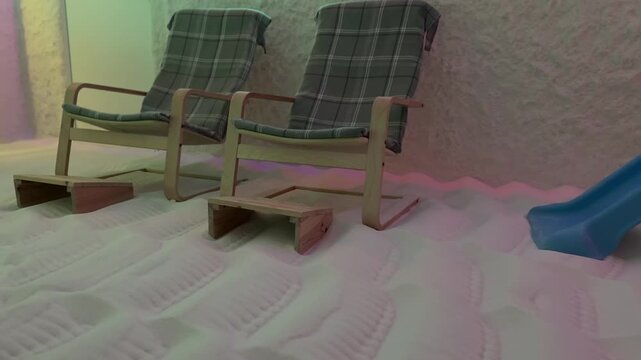 Salt floor wooden chairs halotherapy cave soft pastel lighting casts pink green hues, blue childs slide tucked to side, coarse