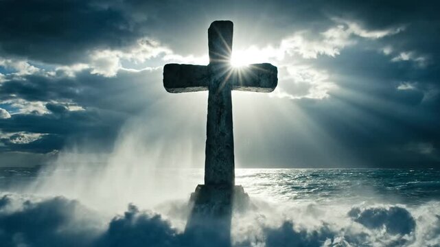 Stone cross silhouetted by sun rays in stormy ocean waters