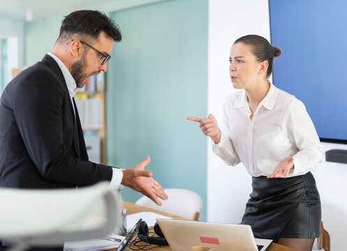 Office employees stand near table and actively argue with each other, they are angry at the inconsistent budget and the wrong project deadlines. Man and woman arguing in the middle of the office
