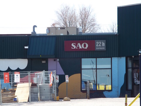 Gatineau, Quebec, Canada &ndash; April 18, 2026: The "SAQ Express" signage is mounted on a colorful storefront next to a construction site with safety fencing and materials on Boulevard Saint-Joseph.