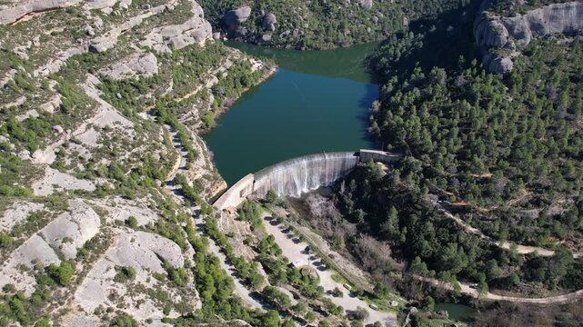Forward reveal aerial footage of Margalef reservoir and dam on sunny winter day. Tarragona Province, Spain.