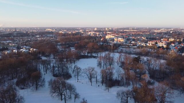 Winter wonderland aerial view of snow covered city park with frozen fields and distant urban skyline