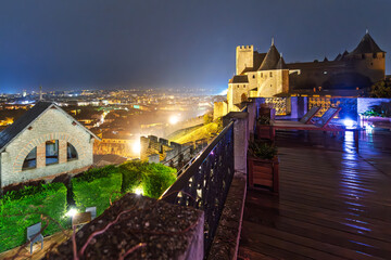 Naklejka premium Late night view overlooking the city and village from inside the medieval fortress and illuminated castle walls of La Cité in Carcassonne, France. 