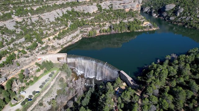 Forward reveal aerial footage of Margalef dam with water flowing through on sunny February day. Tarragona Province, Spain.