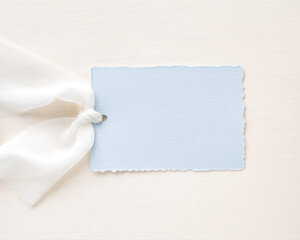 Fototapeta premium Minimal handmade paper tag mockup with soft white ribbon on neutral linen background