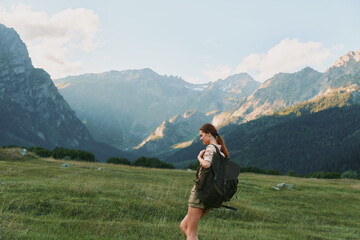 Fototapeta premium Hiker with a large backpack strides across a sunlit alpine meadow under towering mountains, embodying freedom and adventure in a single warm moment
