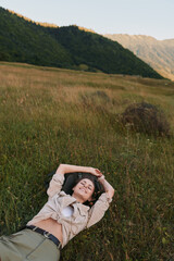 Fototapeta premium A woman lies in a grassy meadow, arms folded behind her head, smiling softly. Broad hills and warm light create a serene outdoor lifestyle portrait today