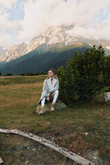 Fototapeta premium Woman sitting outdoors in a mountain landscape, lifestyle portrait with calm mood, wearing a light jacket and boots, amid natural scenery and clear sky