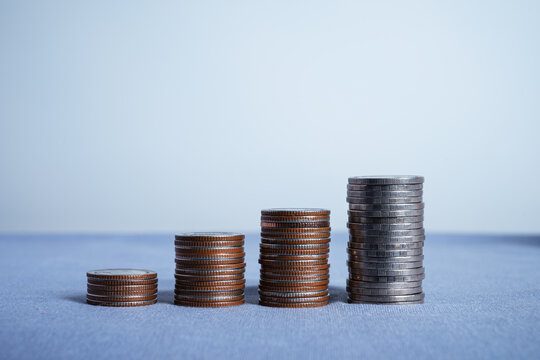 Four stacks of coins arranged in increasing height to represent financial growth and savings. Minimalist concept for investment, banking, and wealth accumulation on a blue surface.