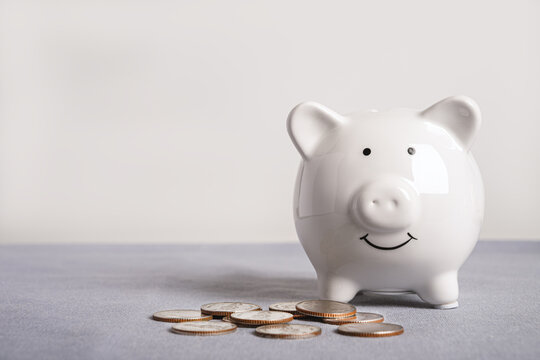 White piggy bank with pile of silver coins on gray surface. Ideal for financial planning, personal savings, banking, and wealth accumulation concepts.
