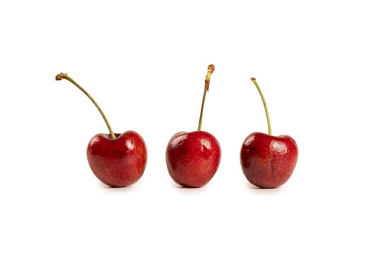 Three vibrant, glossy red cherries joined at the stem isolated on white background.