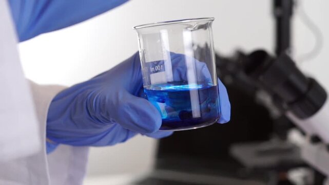 A researcher holds and examines a beaker with a blue liquid sample in a high-tech lab, ideal for concepts related to virology and epidemic prevention.