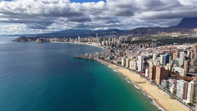 Aerial azure shore and cityscape with crescent beach, highrise clusters, clear turquoise water, mountain