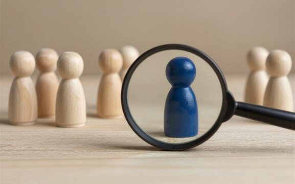 Magnifying glass highlights one blue figurine among many wooden ones.