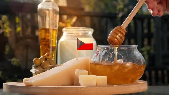 Local Czech honey gently drips from honey dipper beside artisan cheese and dairy goods, with products shown under national flag.