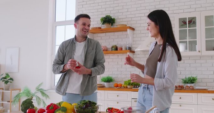 Young happy fit sporty family couple, tomato jongleur fun cooking at home kitchen, green vegetable fresh salad weight loss, healthy eating habits, balanced sport diet, mindful eating, well-being food