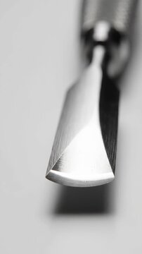 Macro shot of a sharp metal chisel tool with a brushed steel handle and reflective blade displaying precision and craftsmanship for woodworking or sculpting with a clean bright background