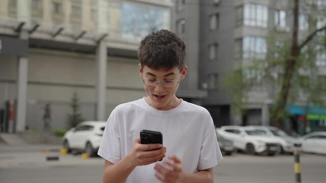 Excited young person reading positive message on smartphone and celebrating success outdoors. Authentic emotions, real people, lifestyle and communication concept.