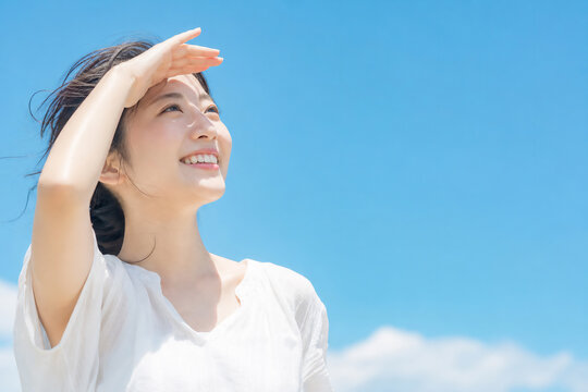 青空の下で眩しそうに目を細め笑顔を浮かべる若い女性 紫外線対策やスキンケアのイメージ Generative AI	