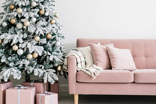 Soft pink couch beside a snowy Christmas tree. Christmas tree with gifts.