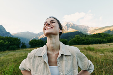 Fototapeta premium Young woman with short hair enjoys fresh mountain air with closed eyes and a smile while standing in a green meadow under a clear sky.