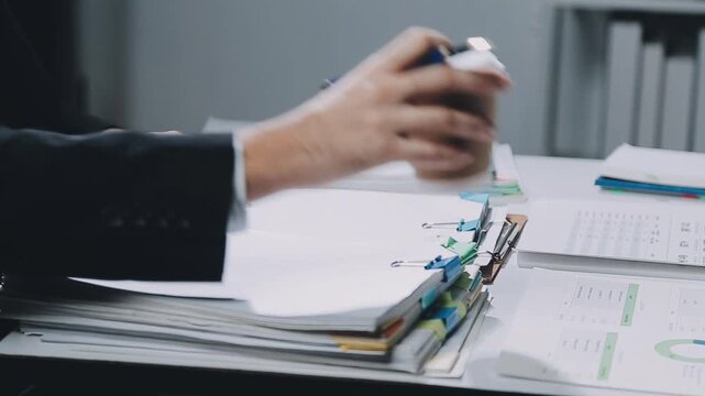 Business professional reviewing important documents at a busy office desk with paperwork and coffee