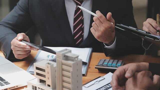 Business professionals discussing real estate contract and property models during a meeting